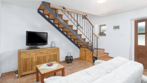 Ein Wohnzimmer mit einer Couch, einem Fernseher auf einer Holzkommode, einer Treppe und einem kleinen Tisch.