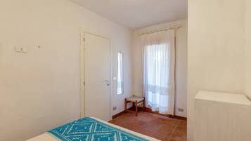 Ein kleiner, sauberer Raum mit einem Bett, einem Sessel, einem Fenster mit Vorhängen und einer Tür.