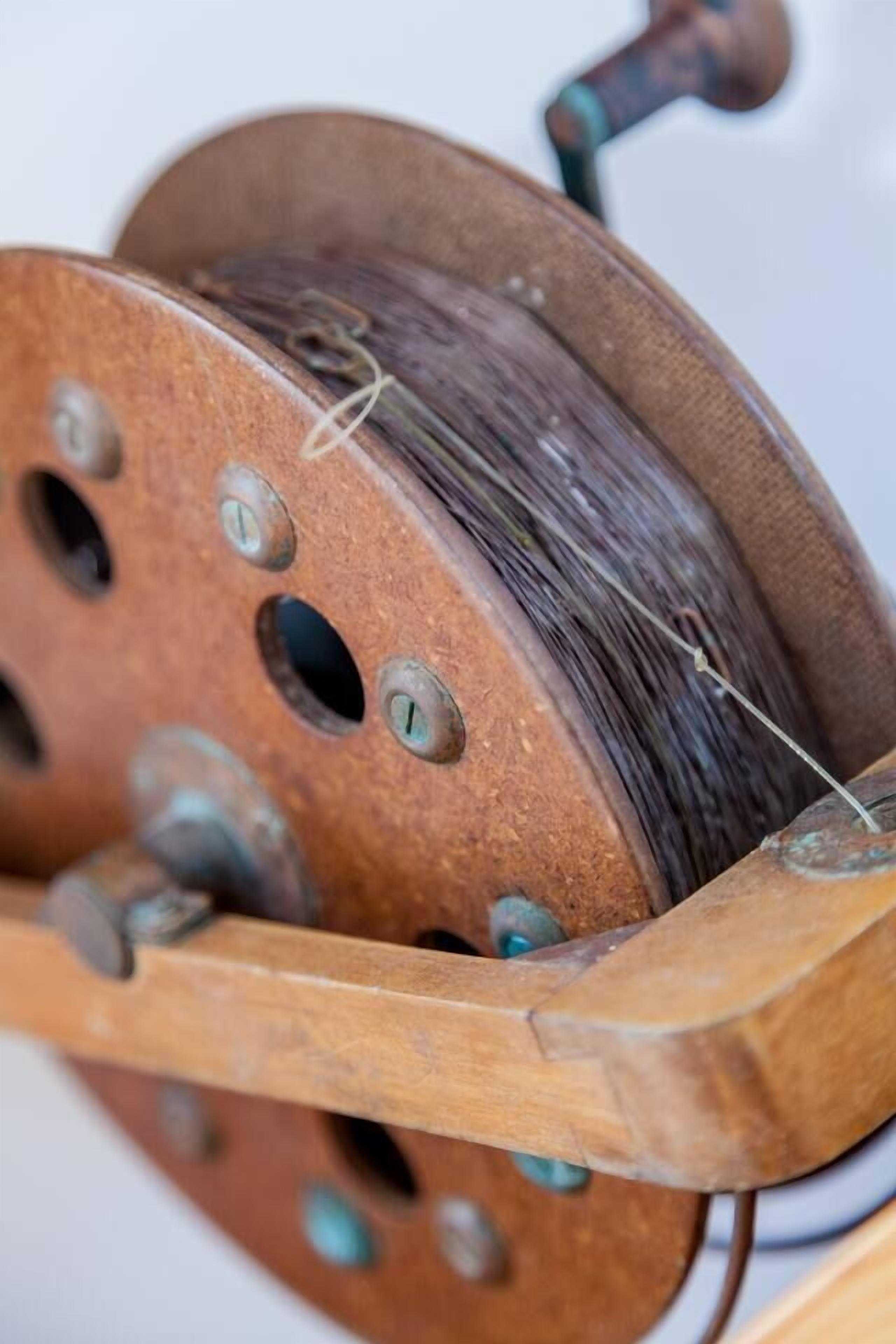 Een detailopname van een houten spoel met een metalen haspel, met zichtbare gaten en een draad.