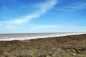 Eine Küstenlandschaft mit einer grünen Fläche, die zum Meer hinabführt, unter blauem Himmel.