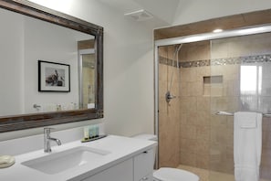 A bathroom with a large mirror, a sink, a toilet, and a shower area.