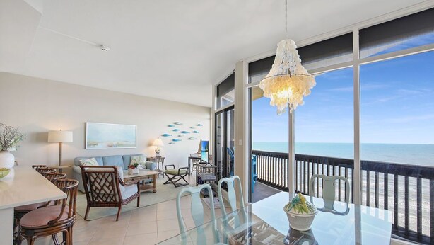 A spacious balcony with a clear view of the ocean, furnished with a glass table and chairs, and a decorative chandelier.