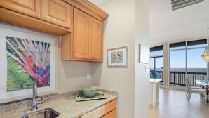 A kitchen with wooden cabinets, a stainless steel sink, and a countertop. There is a framed painting on the wall and a bowl on the counter.