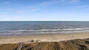 A coastal beach with a sandy shore, a wooden walkway, and a distant view of the ocean.