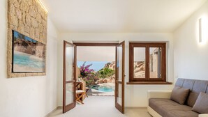 Una sala de estar moderna con vistas a una piscina y zona exterior, que incluye una pared de piedra, un sofá y una mesa de comedor.