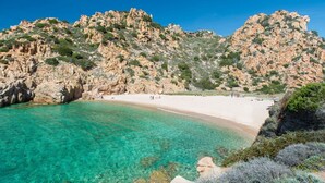 Una playa costera con agua turquesa cristalina, acantilados rocosos y una orilla arenosa.