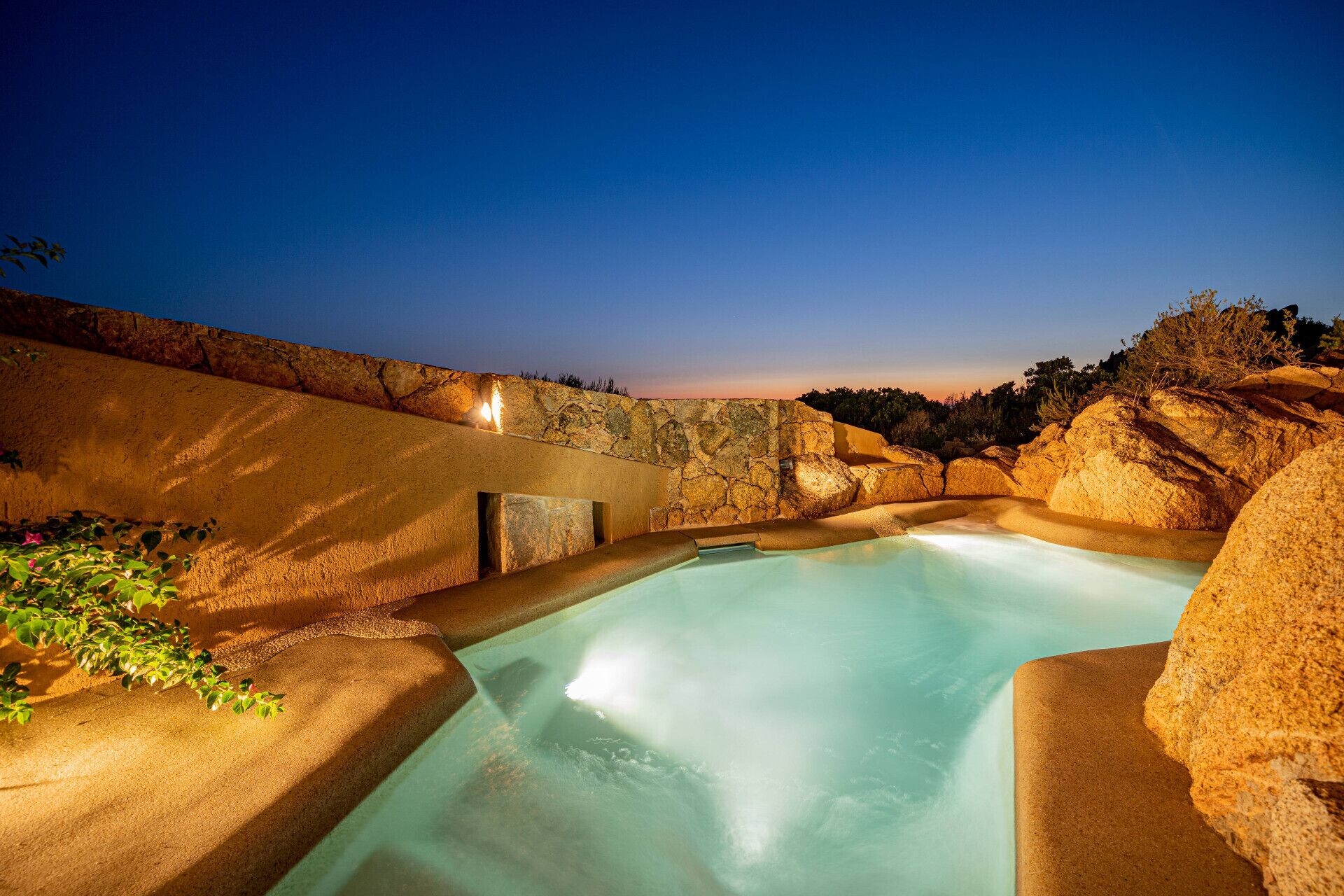Un jacuzzi con pared de piedra y vistas del paisaje circundante.