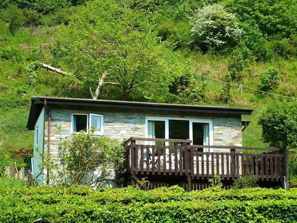 Uma cabana rústica com varanda de madeira, rodeada por vegetação exuberante e árvores.