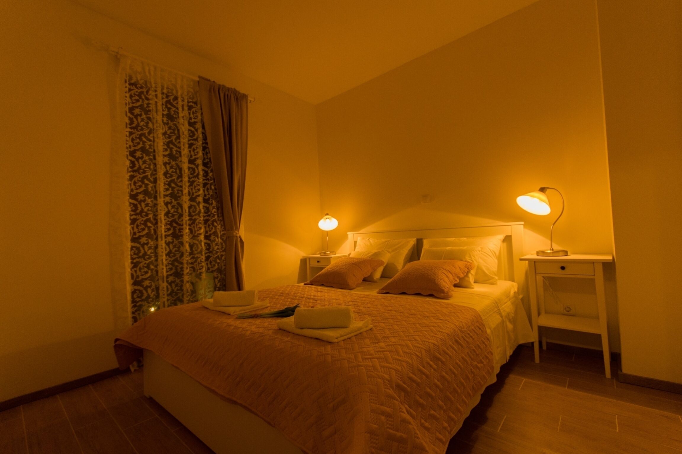 Une chambre à coucher avec un lit, deux tables de chevet, une lampe sur chaque table et une fenêtre avec des rideaux.