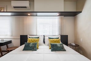 A hotel room with a bed, bedside tables, a desk, and a window with blinds.