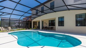 A modern outdoor swimming pool with a glass enclosure, surrounded by a patio area with seating and a covered section. - Veranda Palms IHR 1004 (Kissimmee)