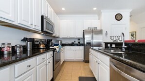 A modern kitchen with white cabinets, stainless steel appliances, and a black countertop. - Veranda Palms IHR 1004 (Kissimmee)