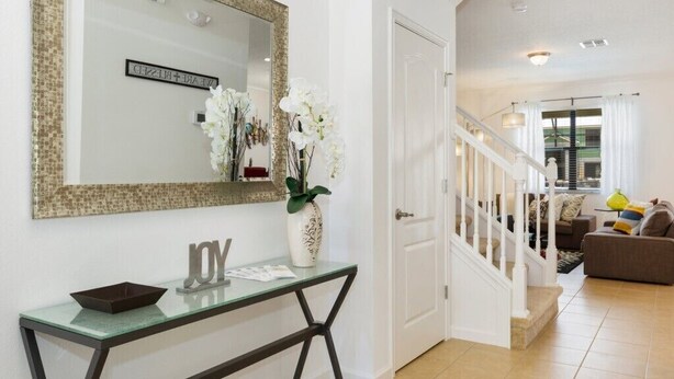 A modern living room with a staircase, a glass console table with decorative items, and a large mirror on the wall. - Veranda Palms IHR 1004 (Kissimmee)