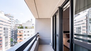 Uma varanda com soalho em mosaico, guarda-corpo preto e vista para edifícios vizinhos.