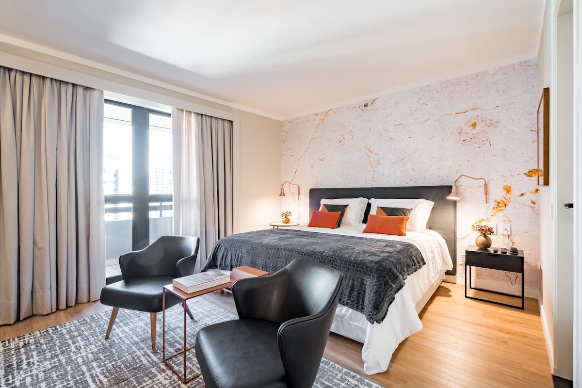 A modern bedroom with a large bed, two chairs, a small table, and a nightstand.