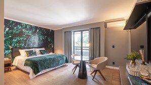 Quarto moderno com cama, mesa redonda, cadeira, janela grande com cortinas e televisão fixada na parede.
