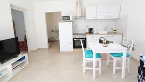 A compact kitchen with white cabinets, a microwave, a stove, and a dining area with a table and chairs. - Apartment Diego & Fabio (Rovinj)