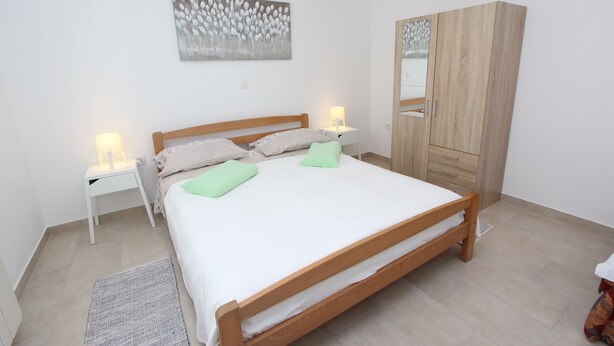 A bedroom with a wooden bed, two bedside tables with lamps, a wardrobe, and a painting on the wall. - Apartment Diego & Fabio (Rovinj)
