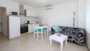 A compact kitchen with white cabinets, a microwave, and a stove. There's a dining area with a white table and chairs, and a black and white patterned sofa. - Apartment Diego & Fabio (Rovinj)