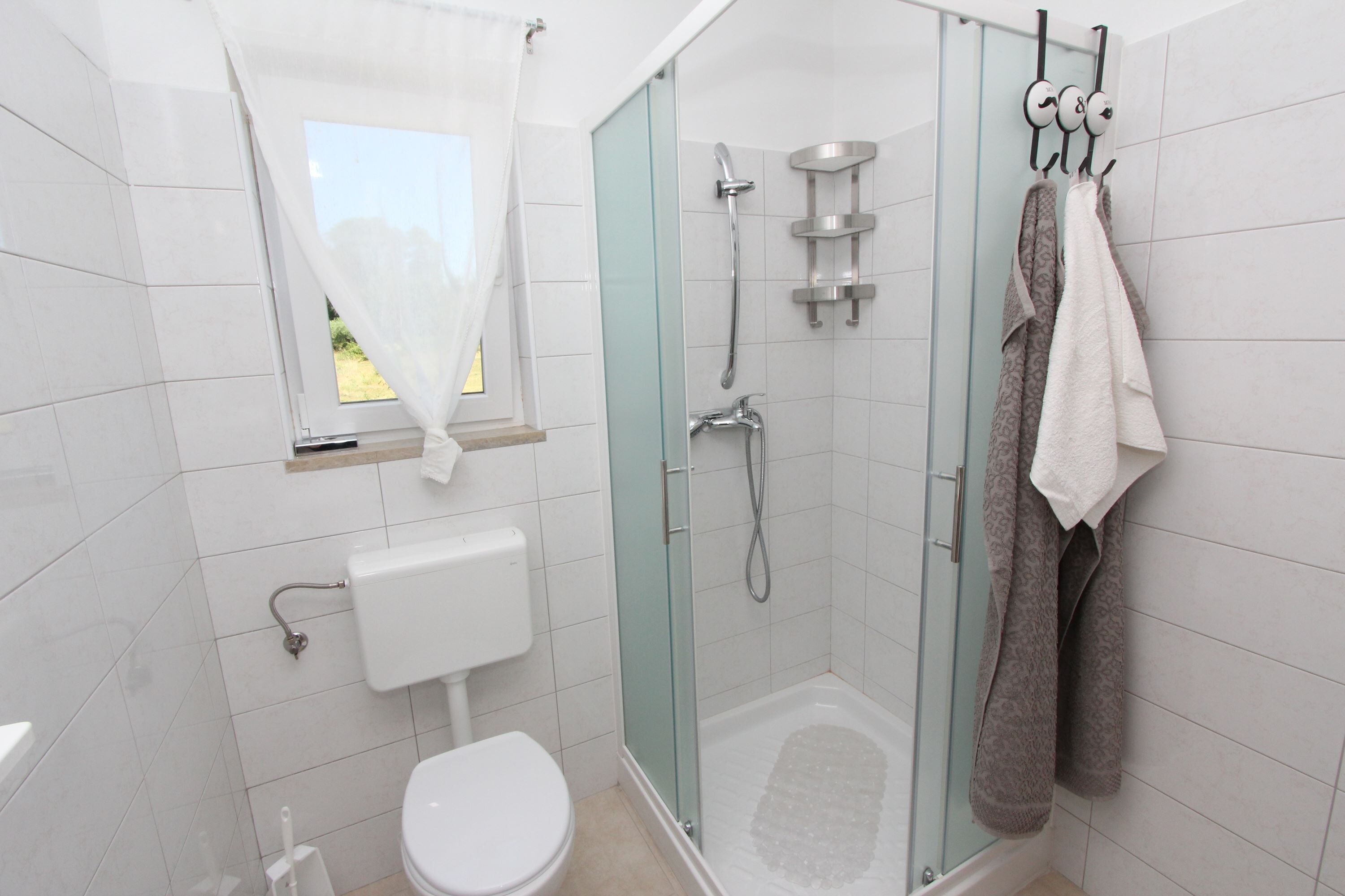 Et moderne badeværelse med bruseniche i glas, toilet og et vindue med gardin.
