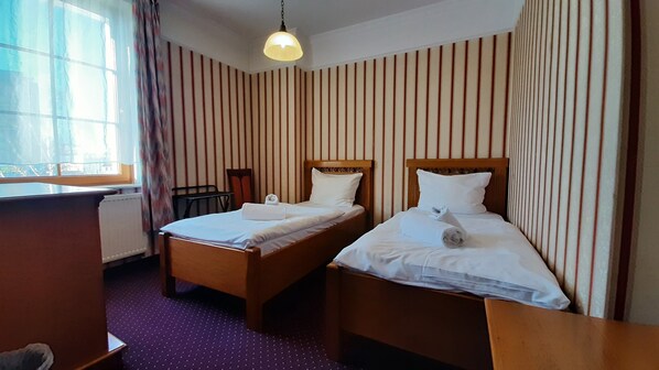 A hotel room with two single beds, a desk, and a chair.