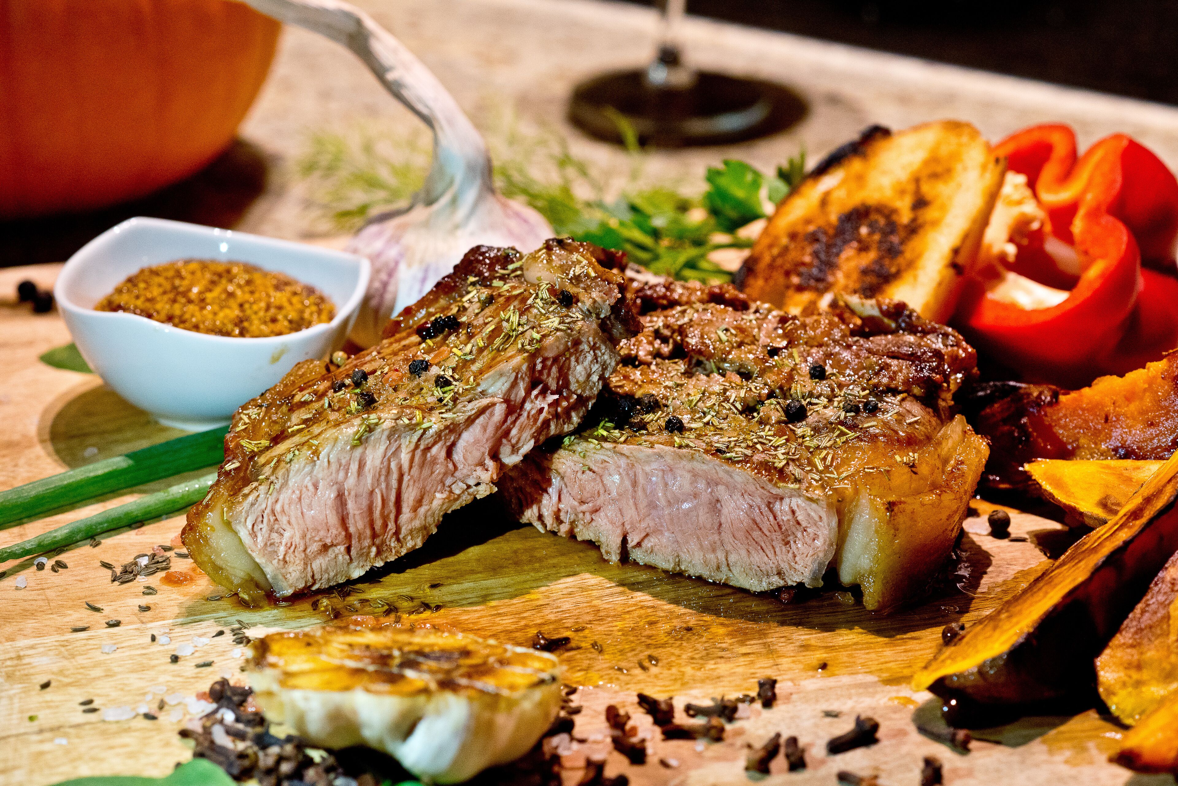 A wooden cutting board with sliced meat, vegetables, and a bowl of seasoning.