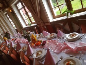 A dining table set with pink napkins, white plates, and clear glasses, with a view of a garden through large windows.