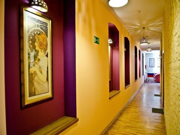 A hotel corridor with purple and yellow walls, framed artwork, and a wooden floor.