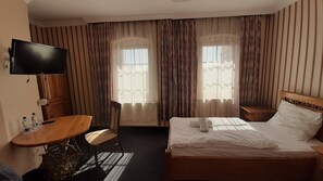 A hotel room with a bed, a desk, a chair, and a television.