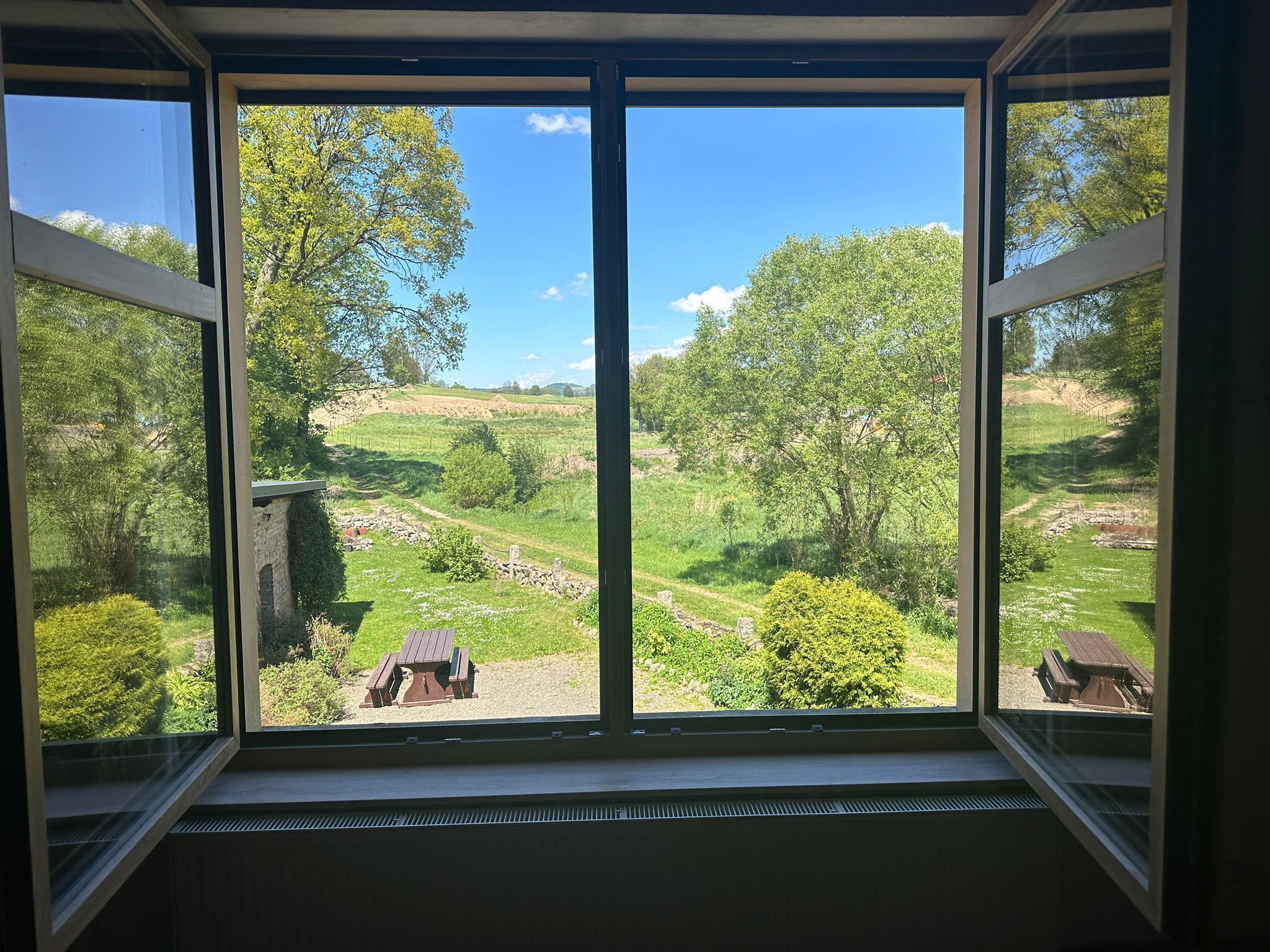 A room with a large window overlooking a green landscape with trees and a clear sky.