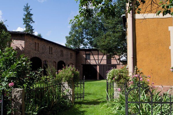 A courtyard with a brick building, a wooden bridge, and a grassy area with flowers.