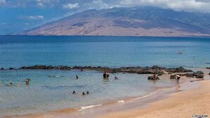 Una playa con aguas cristalinas, afloramientos rocosos y una montaña al fondo.