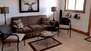 Un soggiorno con un divano marrone, due poltrone, un tavolino da caffè e un quadro con un cervo appeso al muro.