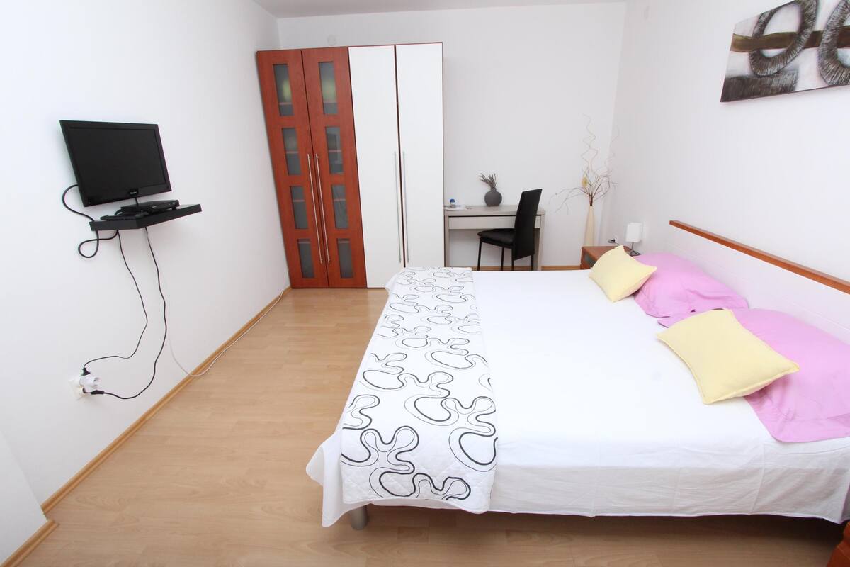 A bedroom with a bed, a desk, a chair, and a television.