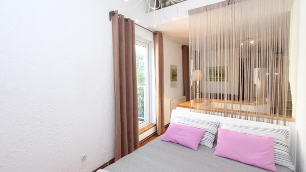 Une chambre à coucher avec un lit, deux oreillers, une fenêtre avec des rideaux et une vue sur l’extérieur.