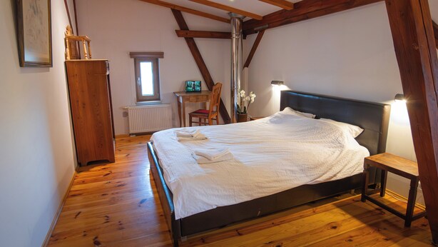 Een slaapkamer met houten vloer, een bed met witte lakens, een houten stoel, een bureau en een radiator.