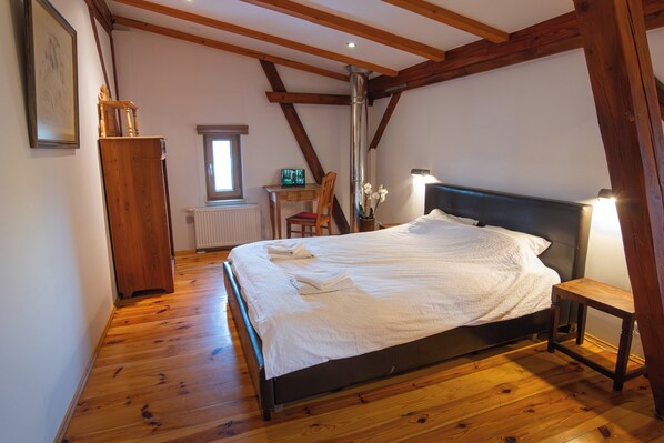 Een slaapkamer met houten vloer, een bed met witte lakens, een houten stoel, een bureau en een radiator.