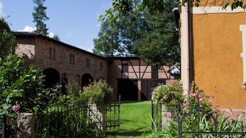 A courtyard with a brick building, a wooden bridge, and a grassy area with flowers.