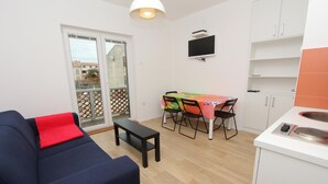 A compact living space with a sofa, a dining table with chairs, a TV mounted on the wall, and a kitchen area with cabinets. - Apartments Paris (Rovinj)