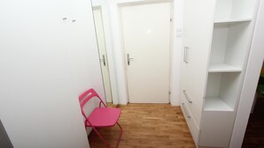 A narrow hallway with a wooden floor, a white door, a pink chair, and a white shelving unit. - Apartments Paris (Rovinj)
