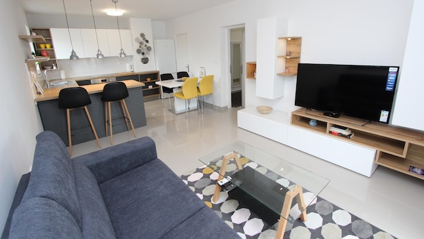 Ein modernes Wohnzimmer mit einem grauen Sofa, einem Glastisch und einem Fernseher auf einem Holzschrank.