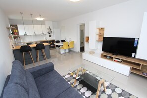 Uma sala de estar moderna com um sofá cinzento, uma mesa de centro de vidro e uma televisão de tela plana sobre um suporte de madeira.