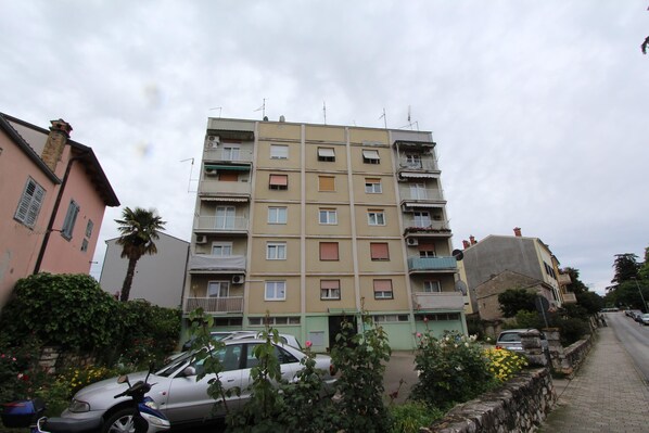 Um edifício residencial com vários andares, varandas, um carro estacionado e um muro de pedra com flores.