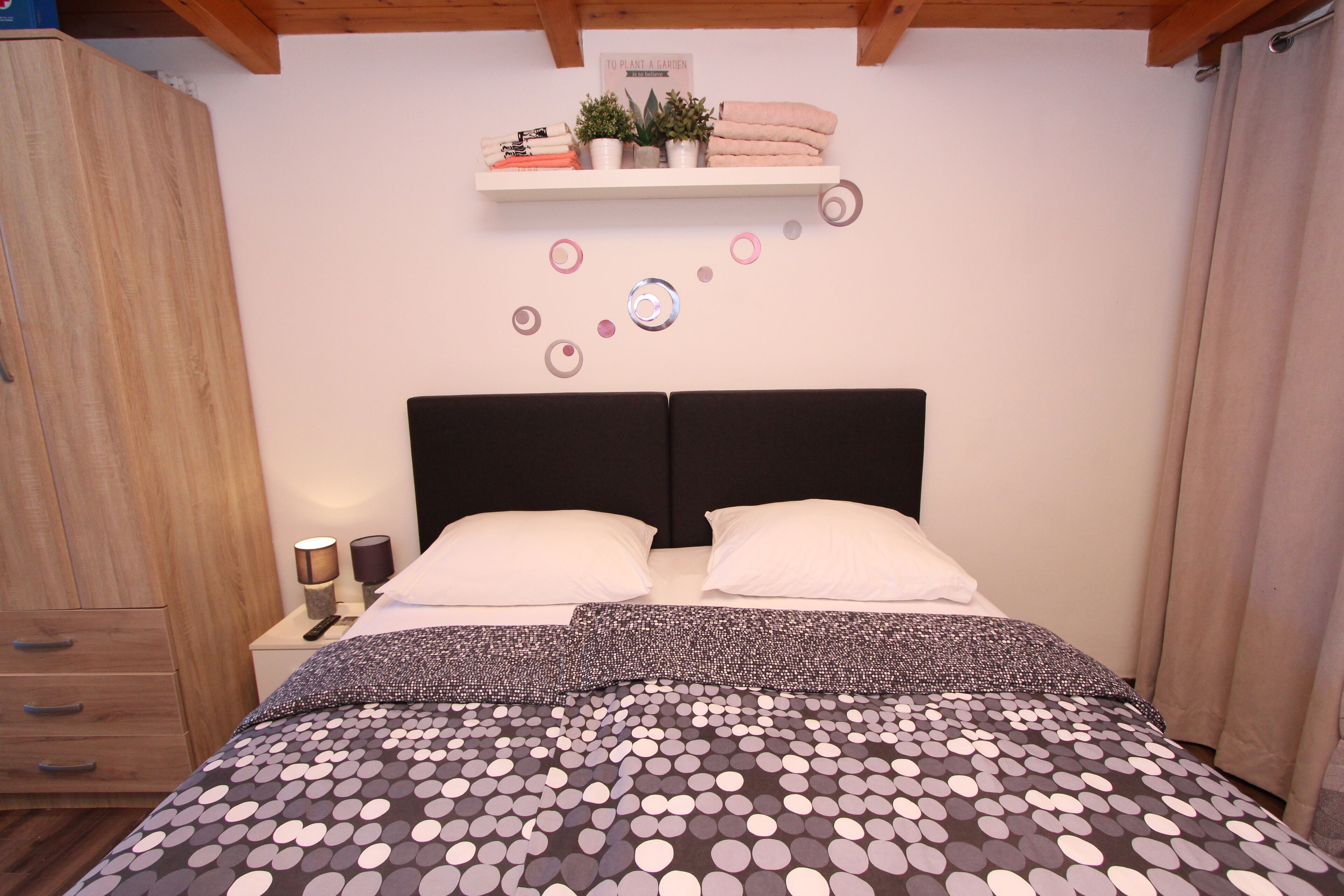 Un dormitorio con una cama, una mesita de noche, un estante con plantas y una decoración en la pared.