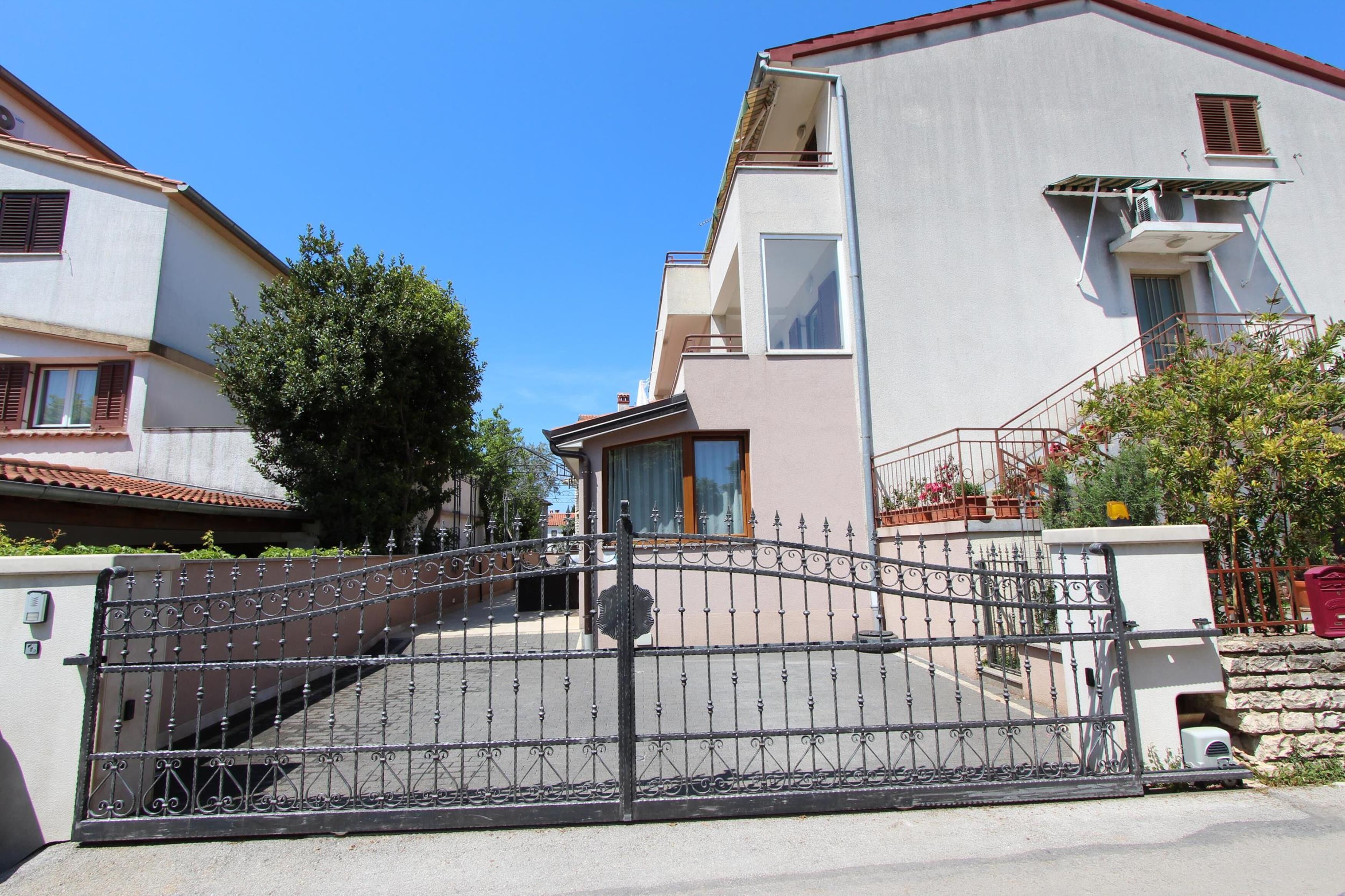 A gated entrance to a residential building with a modern design, featuring a metal gate and a staircase leading to the entrance.