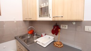 Una cocina con un lavamanos doble, armarios de madera, un escurreplatos blanco y un guante de cocina rojo colgado en la pared.