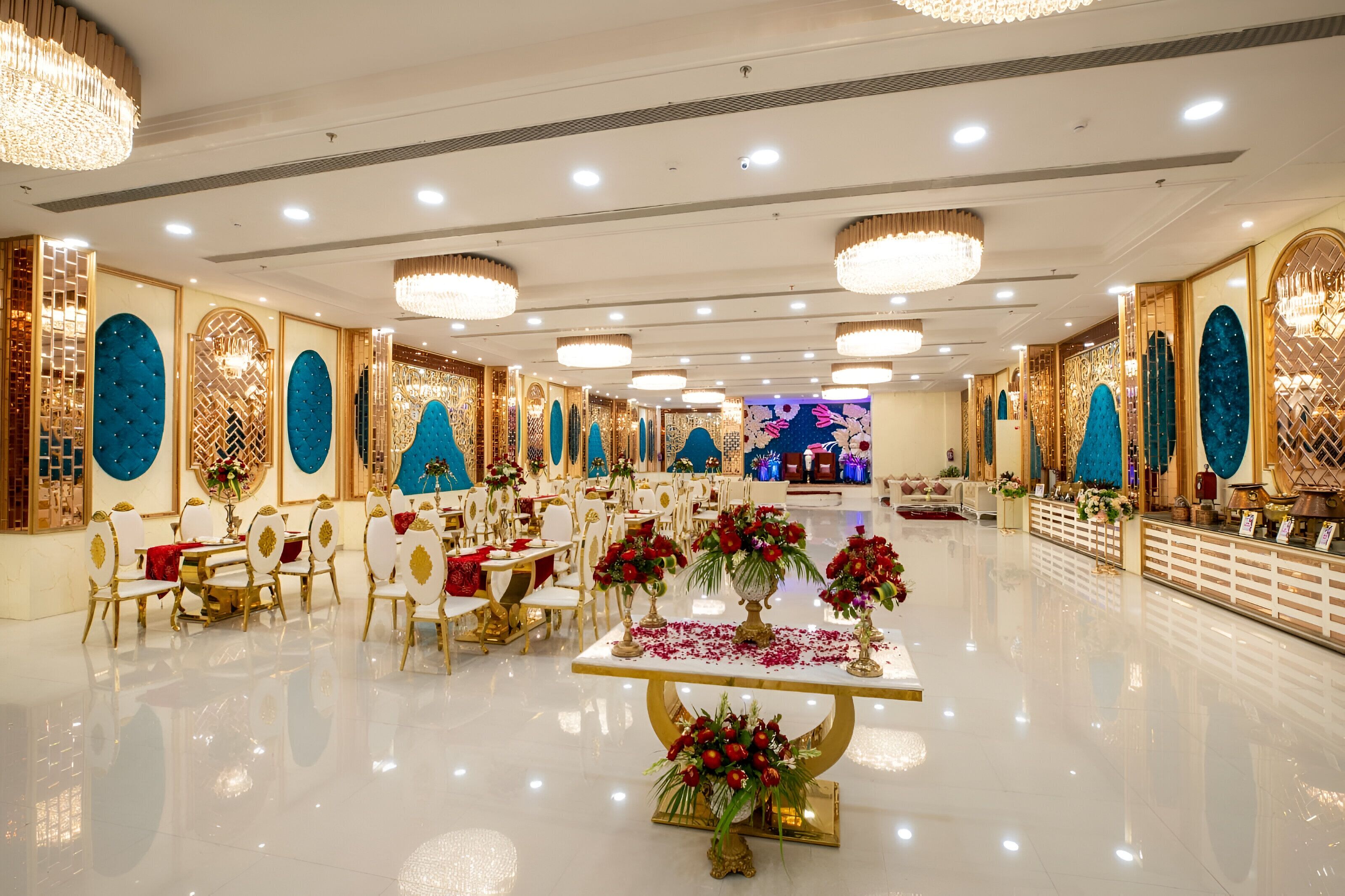 Un amplio y luminoso salón de banquetes con candelabros ornamentados, un arreglo floral central y una larga zona de recepción.
