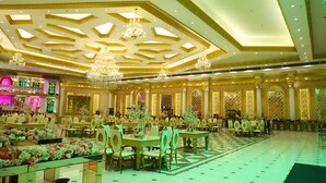 A spacious banquet hall with high ceilings, chandeliers, and ornate wall decorations. Tables are set with floral centerpieces.