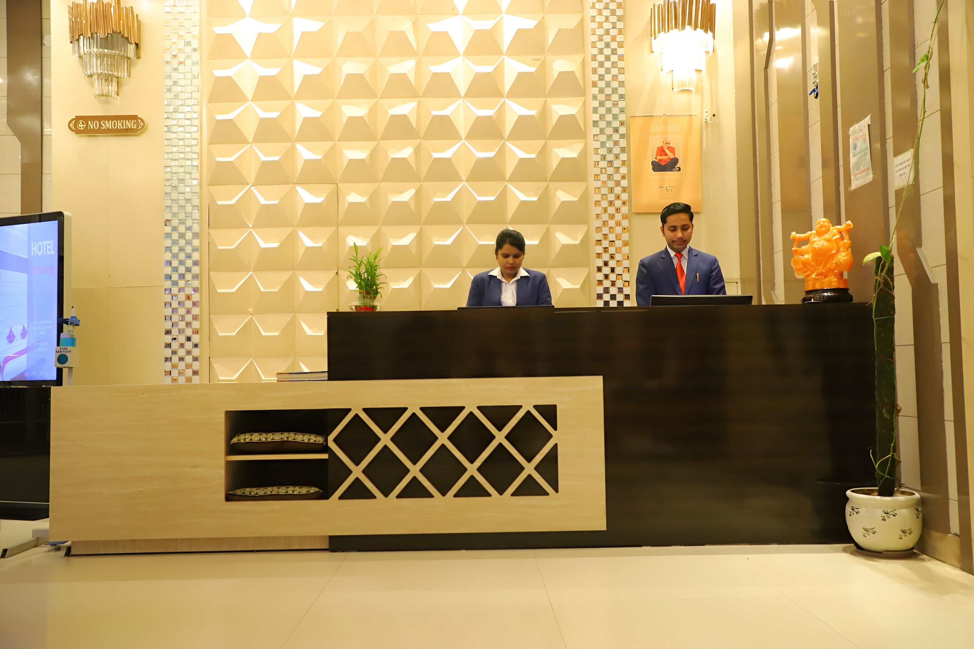 A hotel reception desk with a modern design, a digital screen displaying the hotel name, and a 'No Smoking' sign.