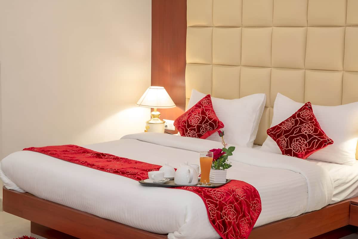 A neatly made bed with white linens, red pillows, and a tray with tea and a glass of orange juice.